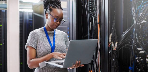 shot of a young woman using a laptop in a server room